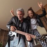 Father rock guitarist having fun and and dancing with his teenage daughter at home.
