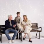 Middle aged couple and dog sitting on bench with a young boy standing and petting the dog.