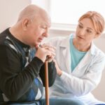 Man with a walking stick being helped by a nurse