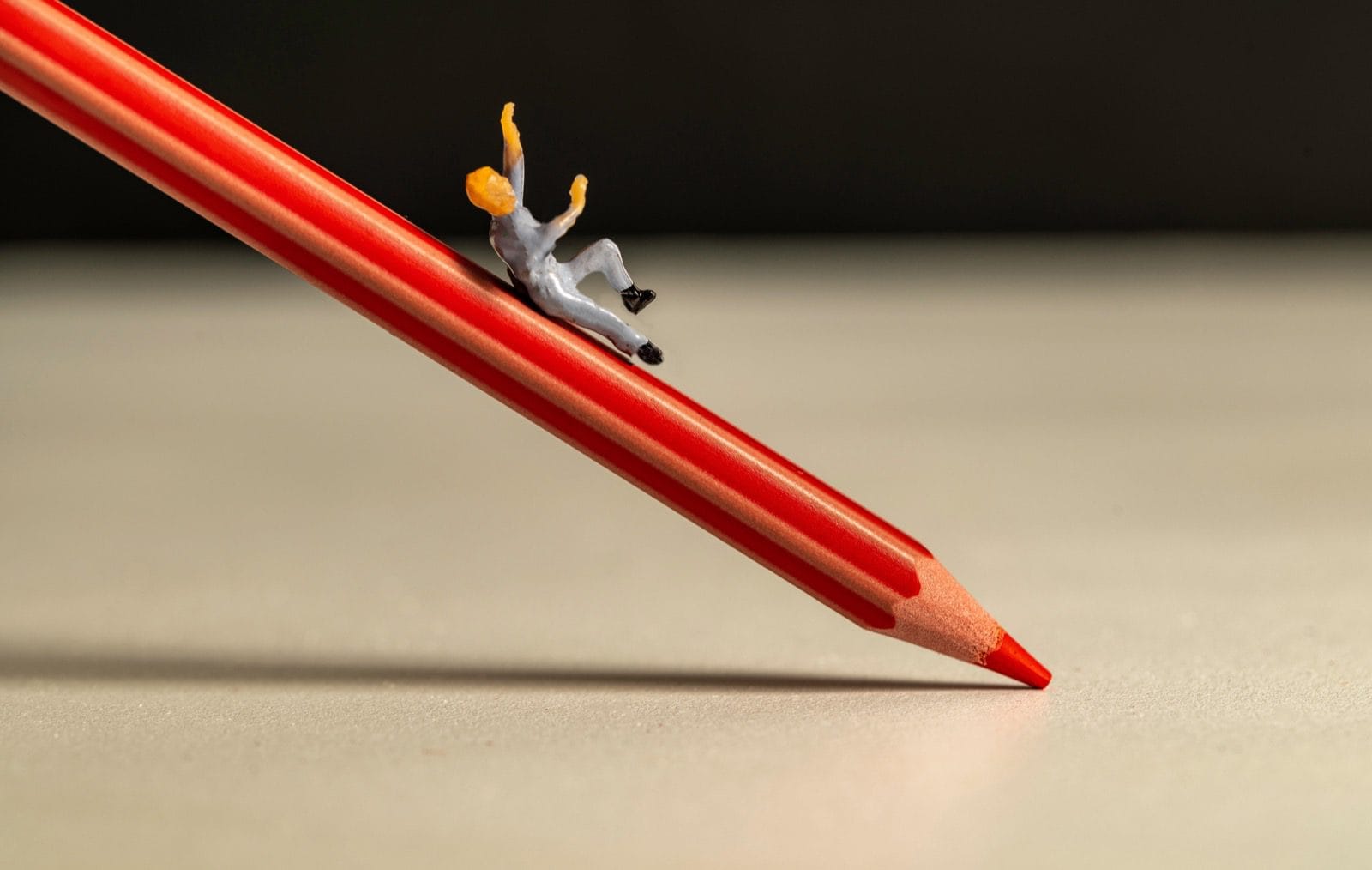Injury on duty. A miniature person slipping down a red pencil.